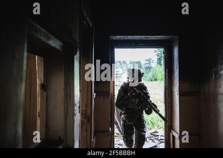 Soldat in voller US MARSOC bewaffnet mit Sturmgewehr durch das verlassene Gebäude laufen. Militärischer Zusammenstoß Stockfoto