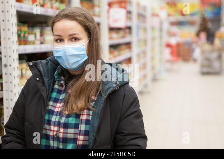 Porträt der kaukasischen Frau trägt medizinische Maske, steht in Hypermarket, warme Kleidung, Kopierer Raum Stockfoto