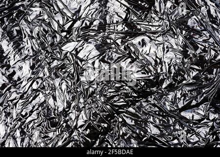 Schwarze Textur aus Verpackungspolyethylen Draufsicht. Abstrakter schwarzer Hintergrund mit Highlights. Zusammengeknüppelte Plastiktüte in Nahaufnahme. Stockfoto