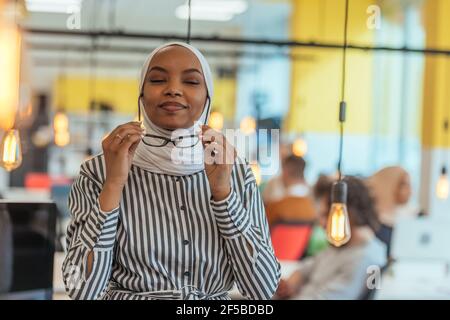 Trait einer schwarzen (afroamerikanischen) weiblichen muslimin, die in einem modernen Geschäftsbüro steht, während sie einen Hijab trägt. Stockfoto