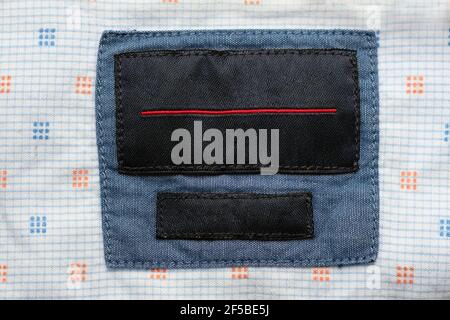 Blaues Denim Baumwoll-Shirt mit leerem Label am Kragen. Unbeschriftete schwarze Beschriftung am Kragen einer blauen Bluse in Nahaufnahme. Stockfoto
