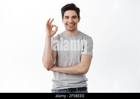 Ich werde mich um alles Ruhe kümmern. Porträt von höflichen gut aussehenden jungen Mann mit Borsten lächeln breit, während zeigt okay oder feine Geste, beruhigend Stockfoto