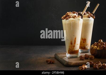 Leckerer Bananenmilchshake garniert mit Karamell, Schlagsahne, Popcorn auf dunklem Grund. Leerzeichen für Text. Stockfoto