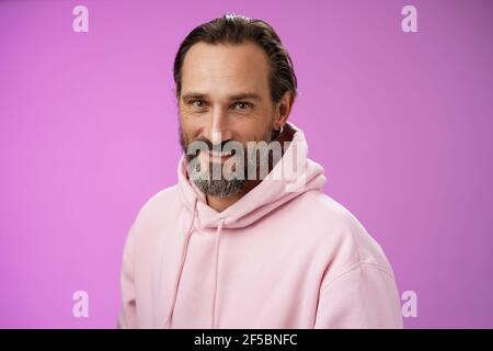 Charming verführerisch gut aussehend bärtig stilvolle Erwachsene männliche Modell Ohrring rosa hoodie Smiling delighted Express Confidence Positivity Fühlen Sie sich glücklich amüsiert Stockfoto