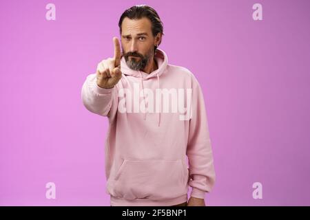 Eine Regel hören. Serious-looking herrisch fokussiert bestimmt erwachsenen bärtigen Mann in rosa Kapuzenpullover verlängern Zeigefinger erste Zahl Schelten Aussage machen Stockfoto