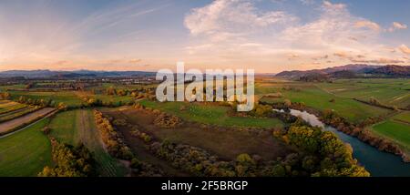 Spektakuläres Luftpanorama des Flusses, der bei Sonnenuntergang durch Felder fließt. Stockfoto