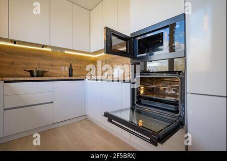 Moderne weiße und beige Holzküche mit Backofen geöffnet Stockfoto