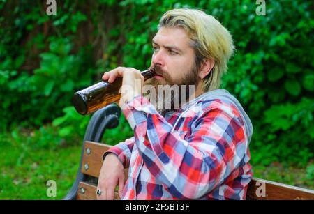 Schöner Mann trinkt Bier in Flaschen. Bärtiger Mann in legerer Kleidung, der im Sommer Bier genießt. Stockfoto