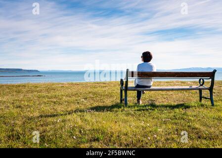 Einsame Frau, die an einem sonnigen Sommertag auf einer bech vor dem Meer sitzt. Konzept der Einsamkeit. Stockfoto