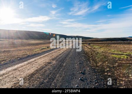 Leere Schotterstraße in einer kargen vulkanischen Landschaft an einem hellen sonnigen Sommertag. Streulicht. Stockfoto