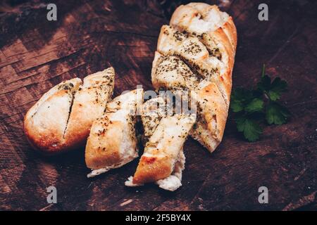 Leckeres Brot mit Knoblauch, Butter und Kräutern auf altem Holztisch Stockfoto