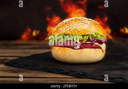 Leckeres Street Food vegetarischer Rote Beete Burger in knusprigem Brötchen mit Salat und Avocado auf schwarzem Steinbrett gegrillt. Stockfoto