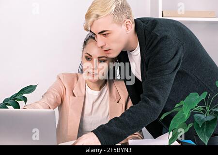 Junge Kollegen Mann und Frau arbeiten im Büro. Fehlende soziale Distanz. Der Mann lehnte sich über die Frau, die am Schreibtisch saß, und schaute auf den Laptop-Monit Stockfoto