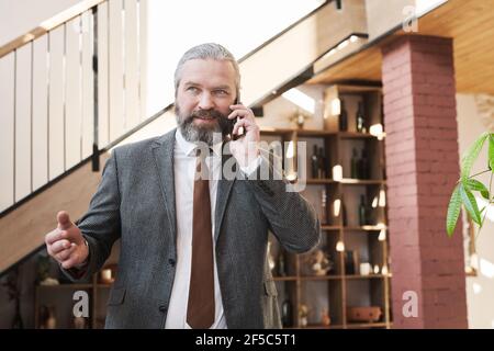 Selbstbewusst reifen Geschäftsmann mit einem Gespräch auf Handy, während Zum Meeting im Restaurant gehen Stockfoto