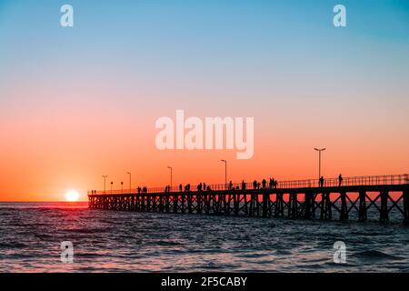 People Silhouetten auf Port Noarlunga Anlegestelle vom Strand bei Sonnenuntergang, South Australia Stockfoto