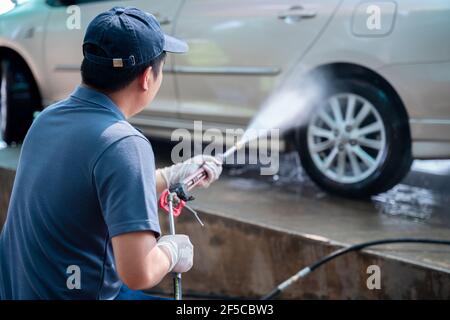 Asian Mann in Uniform Hände wäscht sein Auto mit einem großen Kopf Wasser aus einem karcher und Waschauto mit Seife. Reinigung und Desinfektion. Waschanlage Stockfoto