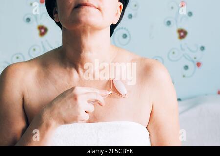 Eine Frau in einem weißen Handtuch macht eine entspannende Gua Sha Massage. Erwachsene Frau Haut Körperpflege Konzept, alternative Medizin und Kosmetologie zu Hause Stockfoto
