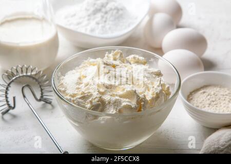 Frischkäse in Glasschüssel Nahaufnahme mit Zucker, Eiern, Mehl und Sahne auf hellem Hintergrund. Zutaten zum Kochen baskischen Spanisch verbrannt Saint Sebastia Stockfoto
