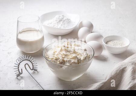 Frischkäse in Glasschüssel Nahaufnahme mit Zucker, Eiern, Mehl und Sahne auf hellem Hintergrund. Zutaten zum Kochen baskischen Spanisch verbrannt Saint Sebastia Stockfoto