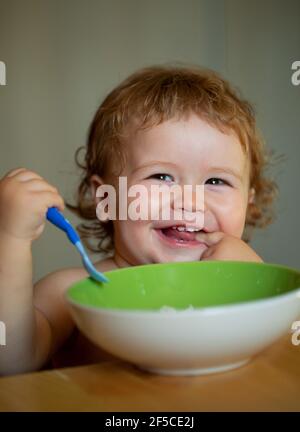 Lächelndes Baby Essen. Lustige Baby Essen selbst mit einem Löffel in der Küche. Gesunde Ernährung für Kinder. Starten Kind essen Nahrung. Stockfoto