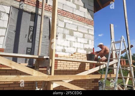 Der Meister stellt das Mauerwerk aus dem vorderen Ziegel, die Erwärmung des Hauses draußen, die Bauarbeiten im Sommer.neu Stockfoto