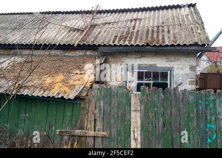 Fassade des verlassenen rickety Backsteinhaus im Dorf hinter grünen Holzzaun. Nahaufnahme. Im Freien. Stockfoto