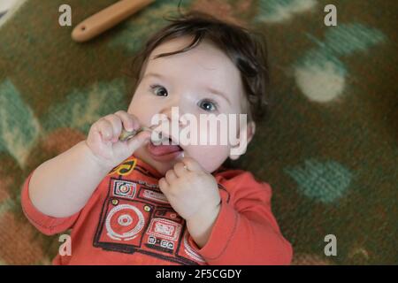 Kind nagt einen Knochen. Ein Jahr altes Baby nagt ein Plastikspielzeug, weil sein Zappen. Kleiner fröhlicher Junge im hellgrünen Anzug mit Schafen. Weichfokus, Boke Stockfoto