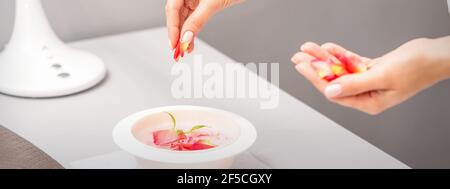 Die weiblichen Hände der Kosmetikerin bereiten das Maniküre-Bad mit Rot und Rosa vor rosenblüten auf dem Tisch im Spa Stockfoto