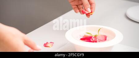 Die weiblichen Hände der Kosmetikerin bereiten das Maniküre-Bad mit Rot und Rosa vor rosenblüten auf dem Tisch im Spa Stockfoto