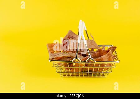 Warenkorb mit Hundefutter auf gelbem Hintergrund. Natürliche getrocknete Kau Leckereien für Haustiere. Stücke getrockneter Kuheuter. Rindfleisch ruckartig für Hunde. Haustierschutz Stockfoto