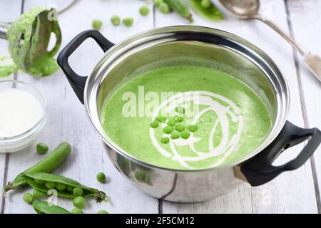 Kochtopf mit frisch gekochter Suppe aus pürierten grünen Erbsen und Sahne auf dem Tisch. Stockfoto