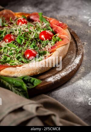 Pizza aus nächster Nähe mit Rucola, Prosciutto und Kirschtomaten auf einem Holzbrett. Foto für das Menü. Stockfoto