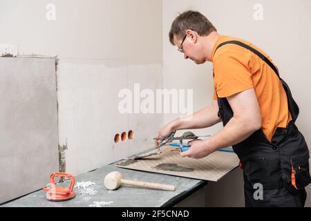 Der Fliesenleger klebt an der Küchenwand, um die Keramikfliesen zu installieren. Stockfoto