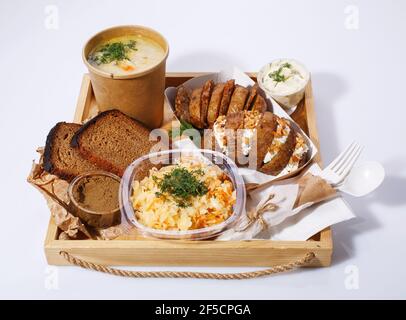 Gemüsesuppe in einer Einweg-Tasse, gebackene Kartoffeln mit Käse und Nüssen in einer Papierbox, Brot, Pastete, Sahnesauce Stockfoto