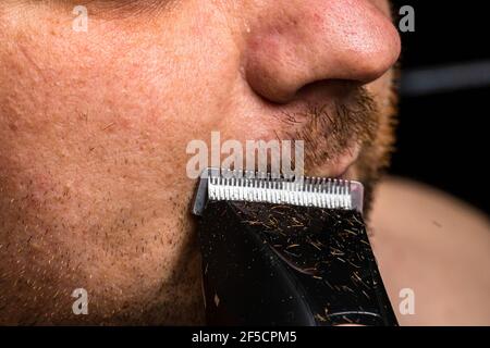 Mann, der seinen Bart mit einem Haarschneider rasiert/trimmt Stockfoto