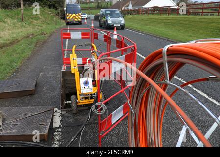 Bei der Installation von ländlichen Glasfaserkabeln außerhalb von Lisburn, Nordirland, Großbritannien, wird eine Rolle Glasfaserkabel in ein Schachtloch eingespeist Stockfoto