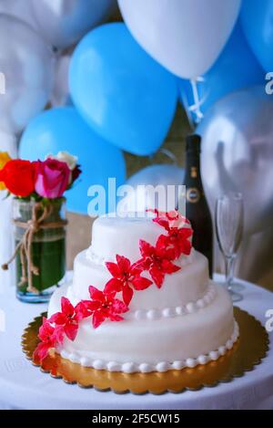 Empfangstisch mit einem eleganten weißen dreistufigen Hochzeitstorte mit zuckerrosa Blumen, einem kleinen bunten Rosenstrauß, einer Flasche Cava und Gläsern Stockfoto