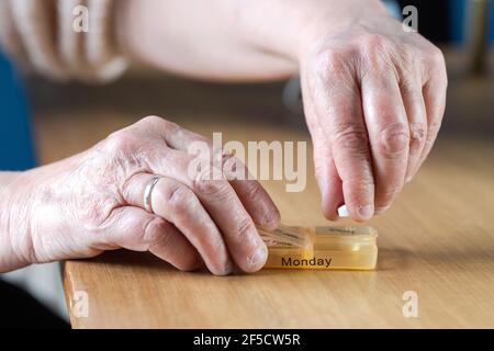 Nahaufnahme der Hände einer älteren älteren älteren Frau, die ihre Medikamente für die Woche in einer Pillenbox auf einem Holztisch einnahm, Geschäfts-, Gesundheits-Konzept Stockfoto