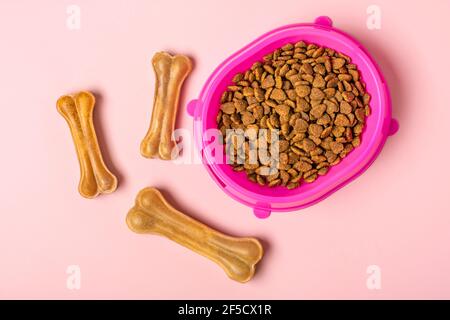 Natürliche Zahnknochen für Hund, trockene Stücke Katze oder Welpenfutter in rosa Kunststoffschale isoliert auf rosa Hintergrund Draufsicht Flat Lay Delicious Leckerbissen für Ihre Stockfoto