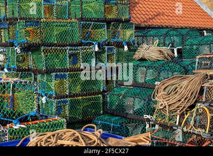 Ein Stapel farbenfroher Hummertöpfe am Kai. Im Vordergrund sind Seile und an einer Seite ein rot gefliestes Dach. Stockfoto