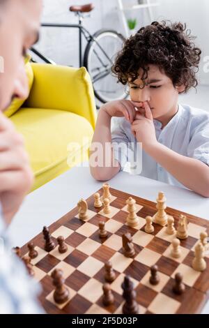 Nachdenklicher arabischer Junge spielt Schach in der Nähe des Vaters auf verschwommenem Vordergrund Stockfoto