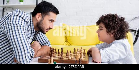 Seitenansicht von arabischem Vater und Sohn, die zu Hause Schach spielen, Banner Stockfoto