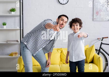 Fröhlicher arabischer Mann und Sohn kleben Zungen und zeigen mit Finger beim Betrachen der Kamera Stockfoto