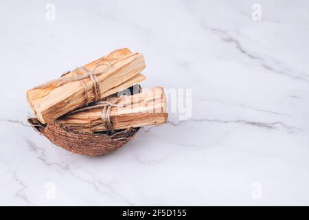 Palo Santo Baum klebt in Kokosnussschale auf hellem Marmorhintergrund - heiliger Weihrauchbaum aus Lateinamerika. Meditation, geistige Gesundheit und persönlich Stockfoto