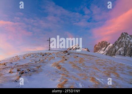 Bergkreuz auf einem schneebedeckten Gipfel während des Übergangs zwischen der goldenen und blauen Stunde bei Sonnenuntergang. Sulzenschneid, Filzmoos, Salzburg Stockfoto