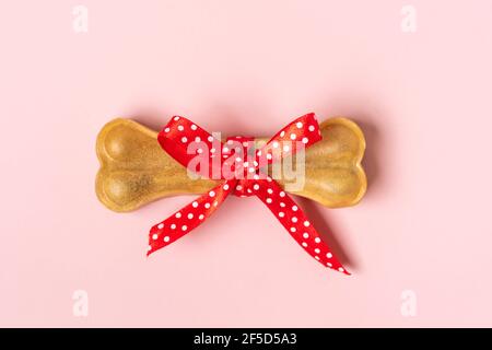 Knochen für Hunde mit roter Schleife isoliert auf rosa Hintergrund Draufsicht Flat Lay Delicious Leckerbissen für Ihr geliebtes Haustier Food for Animals Konzept Stockfoto