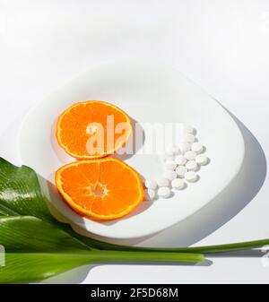 Die orangefarbenen Kreise sind als Zahl acht auf einer weißen Platte gefaltet. Weiße runde Pillen und grüne Blätter. Stockfoto