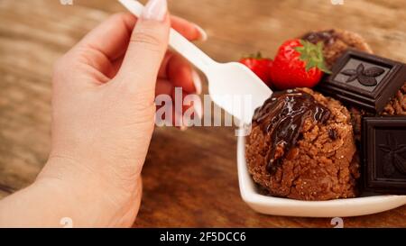 Hand mit einem Löffel. Hausgemachtes Schokoladeneis mit Schokolade und Erdbeeren Stockfoto