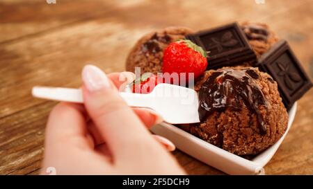 Hand mit einem Löffel. Hausgemachtes Schokoladeneis mit Schokolade und Erdbeeren Stockfoto