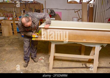 Arbeiter in der Schreinerei verwendet professionelle manuelle Elektrowerkzeug, acu-Bohrer, und dreht die Schrauben auf dem hölzernen Türrahmen. Stockfoto